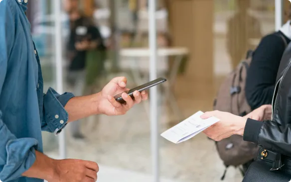 Personne remettant un billet imprimé à une autre personne tout en tenant un smartphone, illustrant l'utilisation d'imprimantes à cartes et billets thermiques.