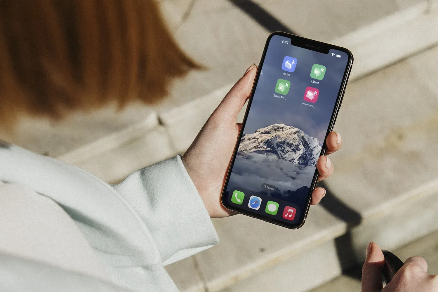 Photo d'une main tenant un smartphone affichant un écran d'accueil avec des icônes d'applications kSuite, sur un fond d'image de montagne enneigée.