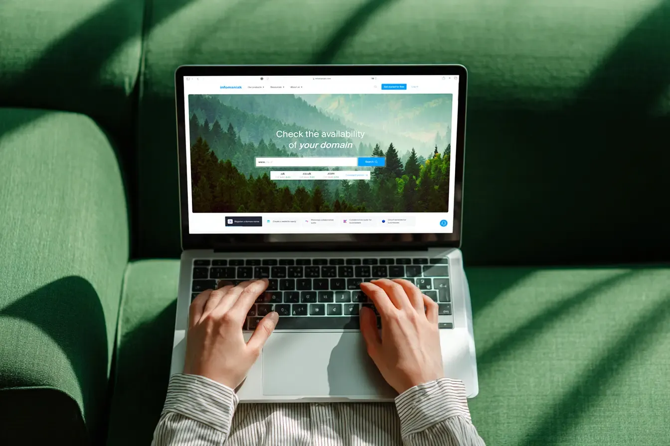 Vue de dessus des mains d'une personne tapant sur un ordinateur portable affichant le site d'Infomaniak