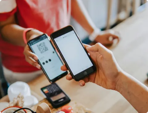 Personne utilisant un smartphone pour scanner un QR code sur un autre téléphone, symbolisant un guichet de vente moderne et numérique.